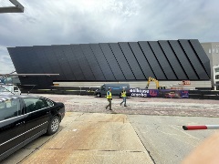 Wide shot of construction workers walking along the newly installed black steel cladding.