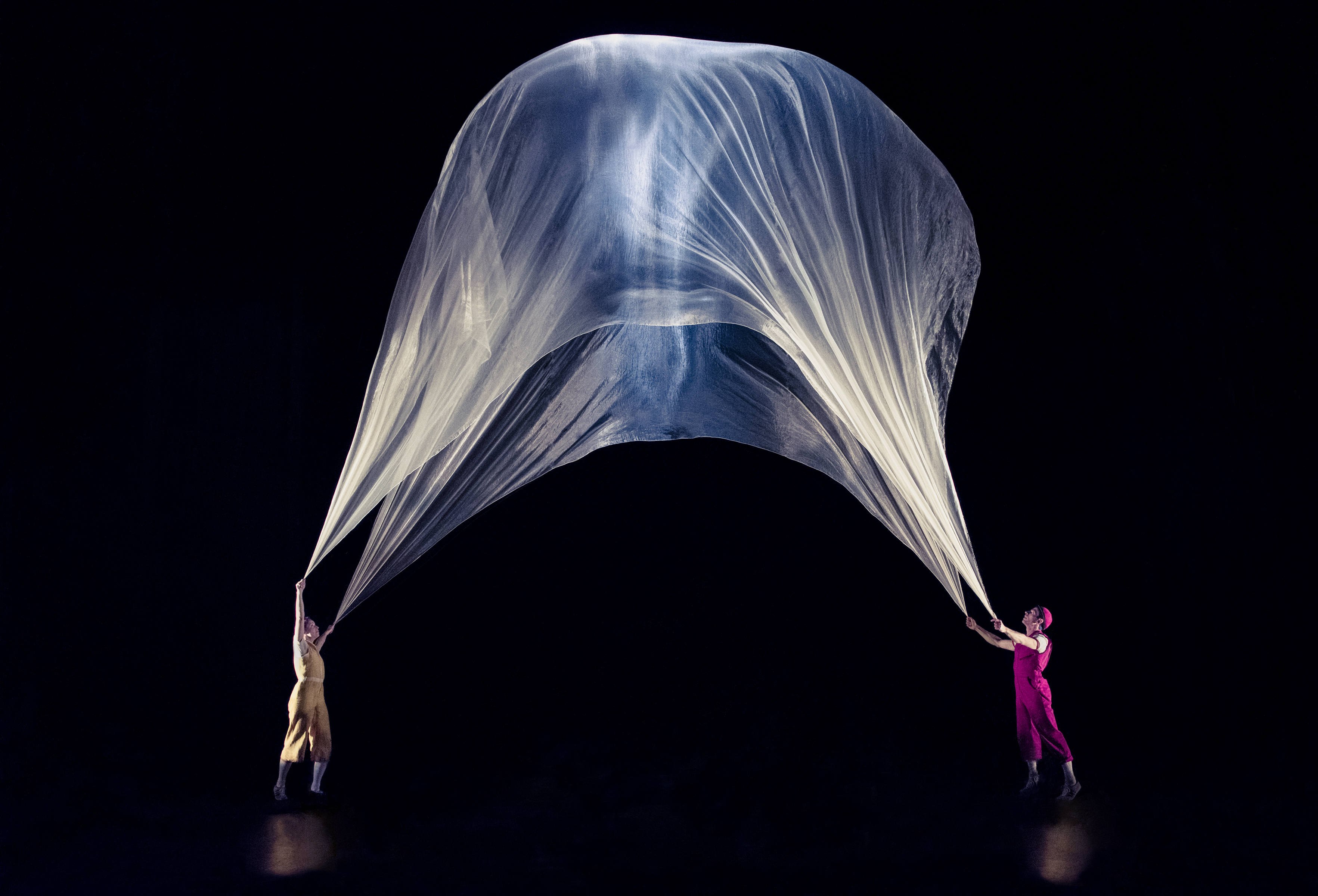 Two performers hold a huge white piece of fabric that billows high above their heads.