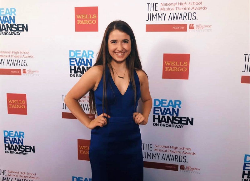 Teen girl in a blue dress smiles as she poses on the red carpet