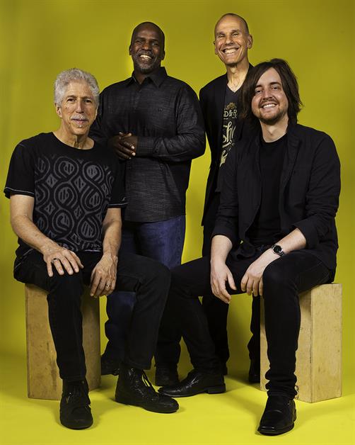 Four men sit against a yellow background