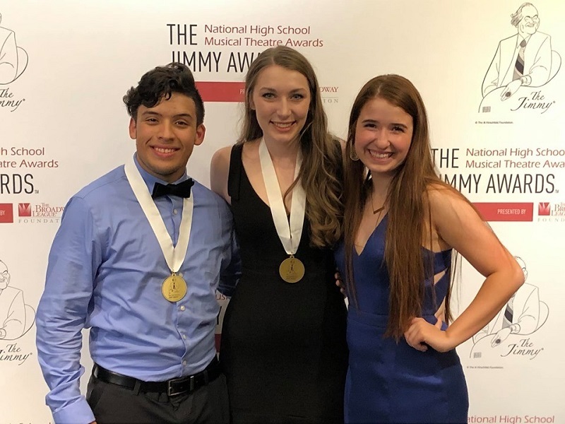 Three young adults in formal wear pose together with medals around their necks.