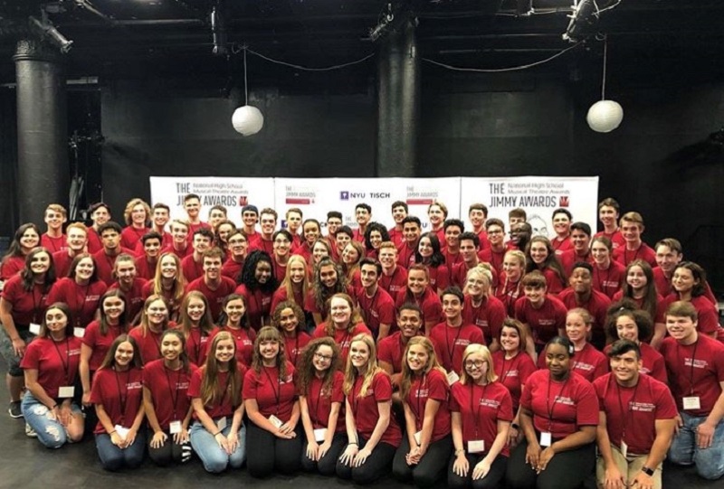 A large group of young performers in red t-shirts gather for a photo.