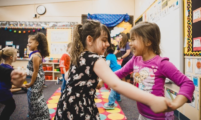 Two second-grade girls hold hands and dance to music in their brightly colored classroom during a Musical Explorers lesson. 