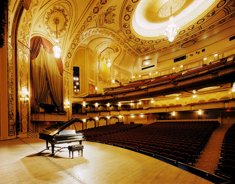 An empty auditorium with lights on and piano on stage