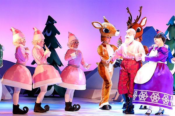 Actors on stage dressed as characters from Rudolph including santa, elves and reindeer