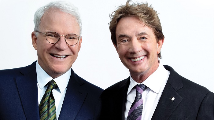 Steve Martin and Martin Short stand together for a photo. They're wearing suits, smiling, standing against a white backdrop.