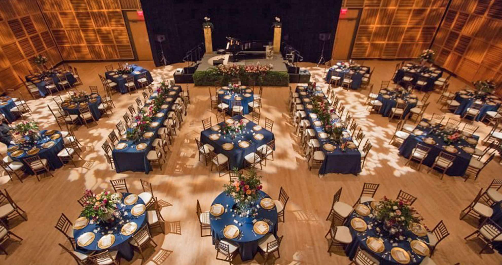 round tables with blue tablecloths, center pieces and decor set up in a room for a reception