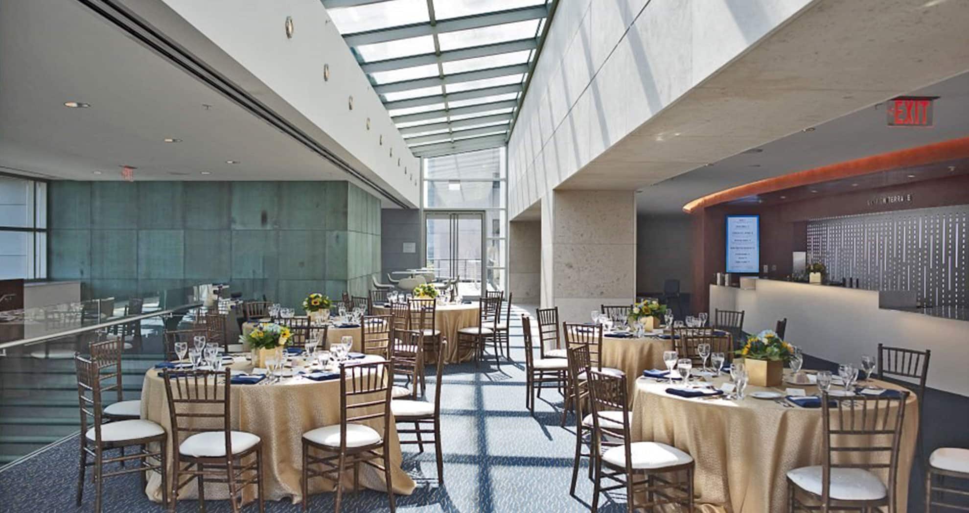 wedding reception set in a lobby with skylights overhead. round tables with cream table cloths and brown chairs.