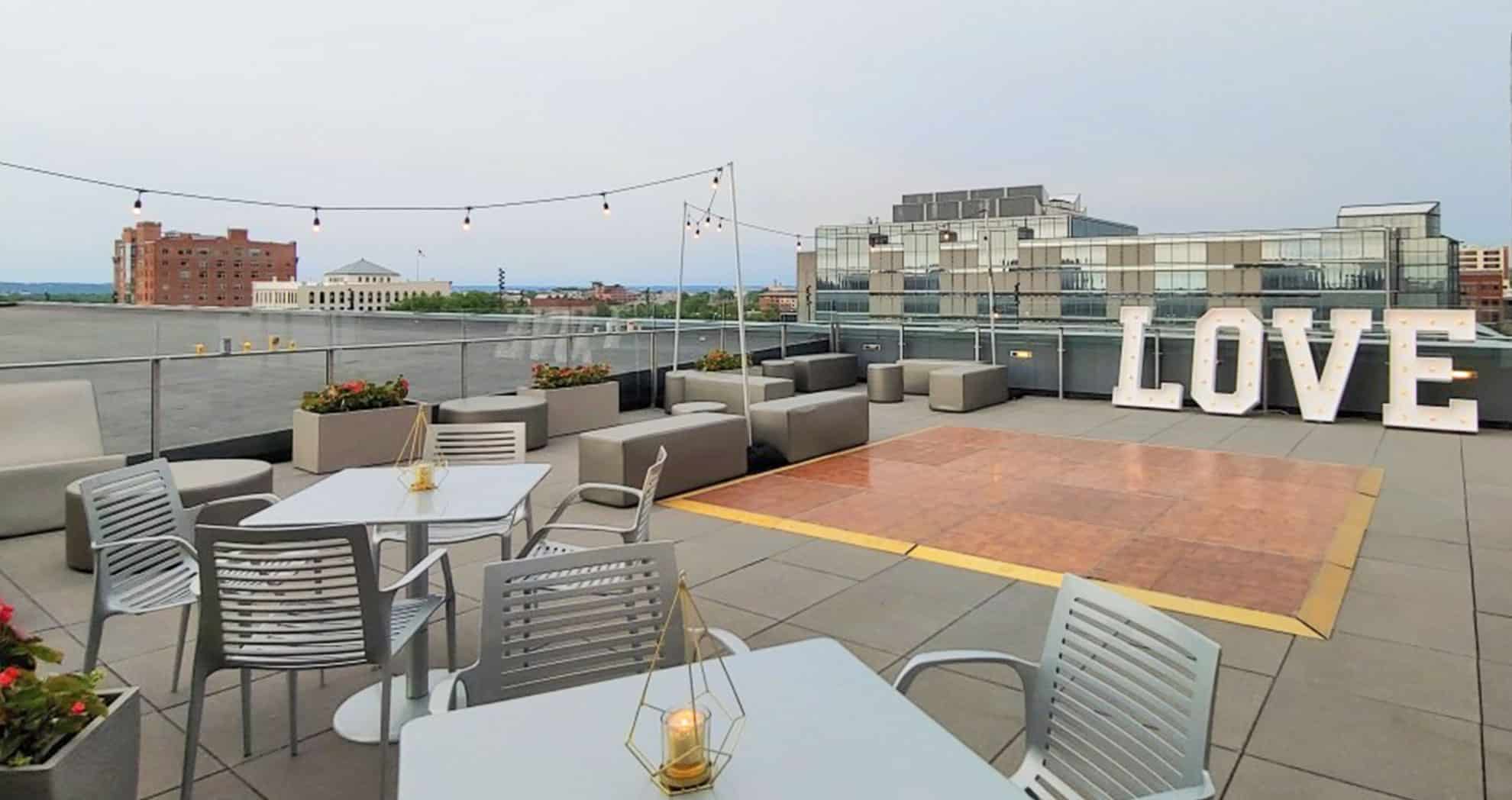 an event set up on a rooftop patio with a dance floor, strong lights not on and metal tables that seat 4