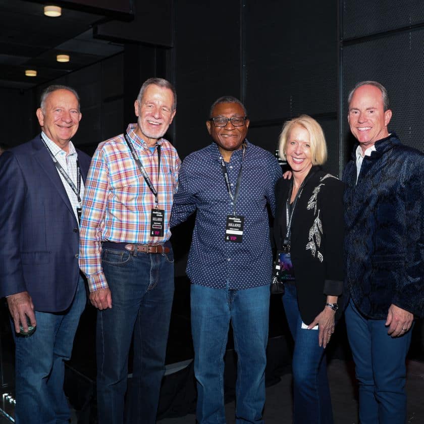 4 men and a woman stand together smiling at a concert