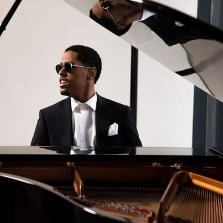 young black man with sunglasses on sits at a pino