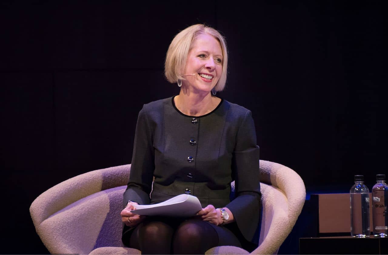 a woman seated on stage presenting with a script in her lap