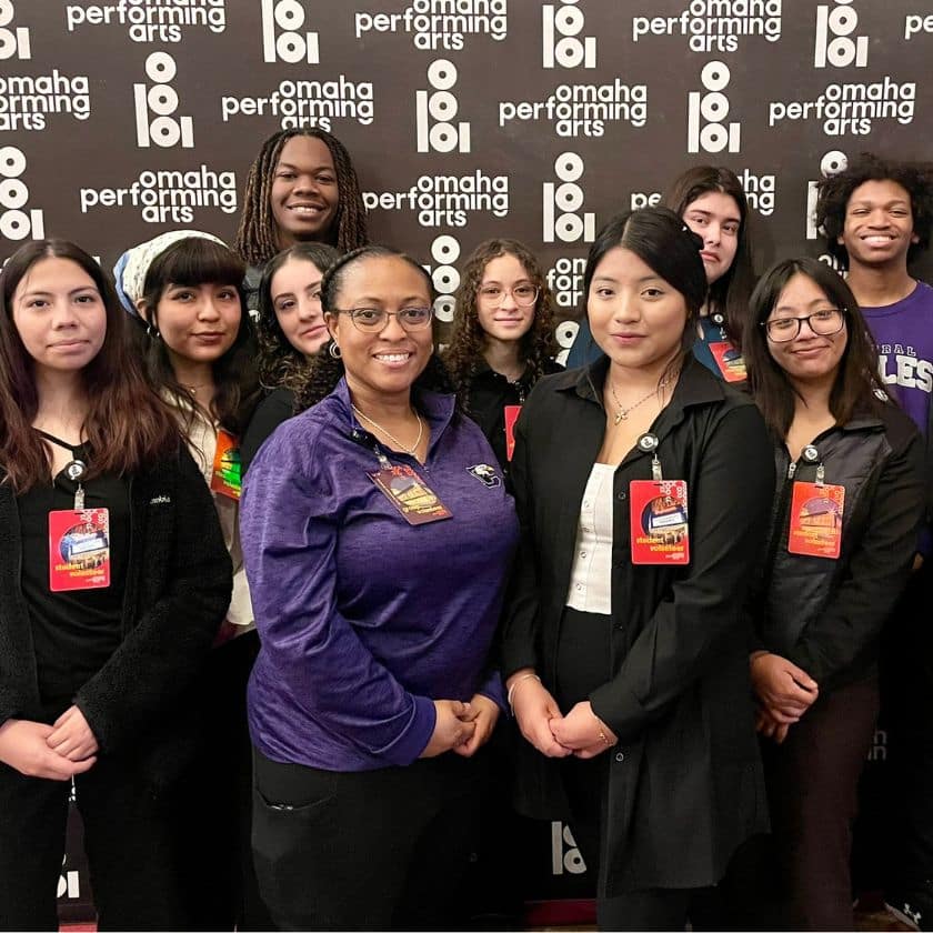 a group of high school students and a teacher posed together for a group photo in front of a backdrop that reads omaha performing arts