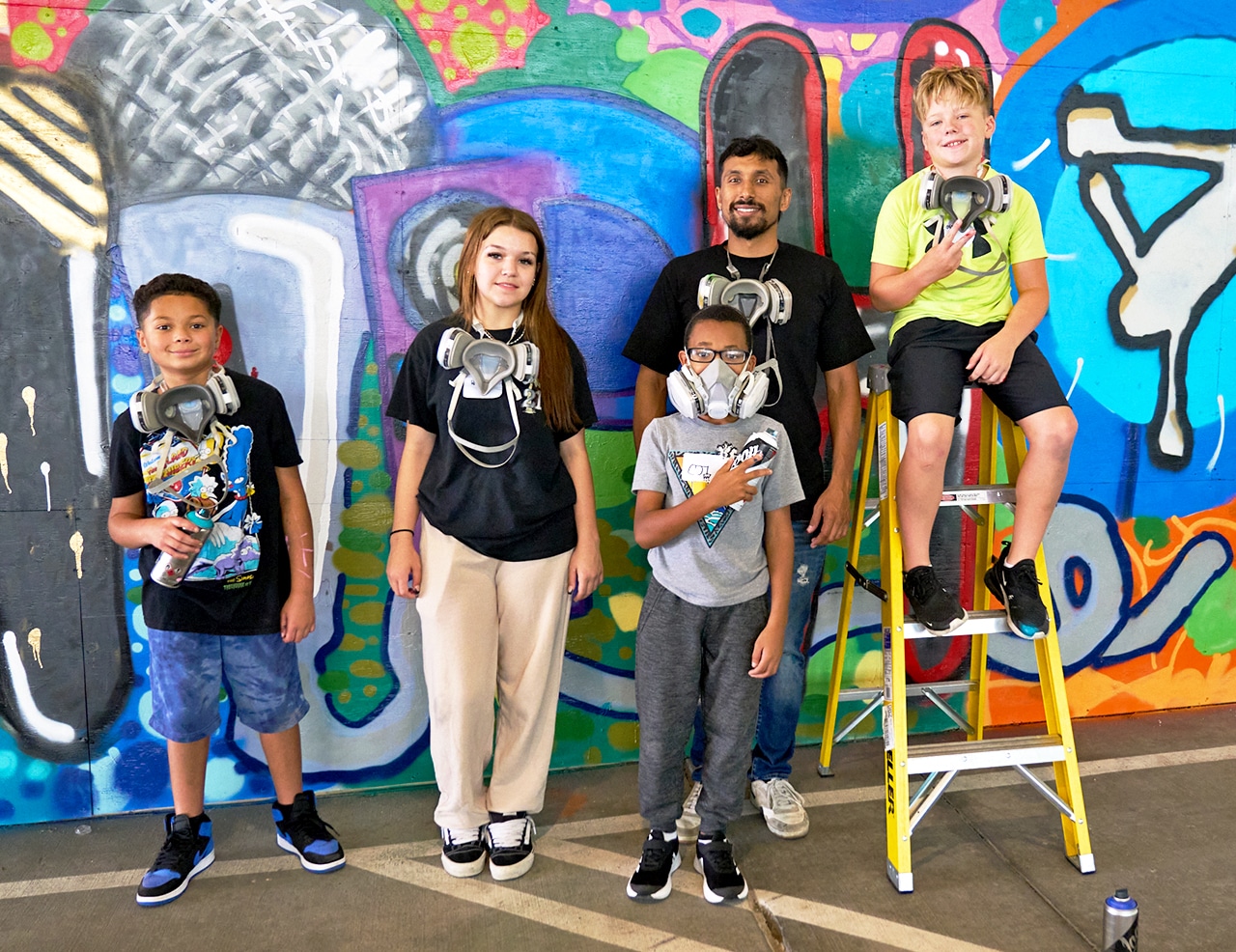 Graffiti Artist with a group of kids standing in front of a colorful spray paint mural