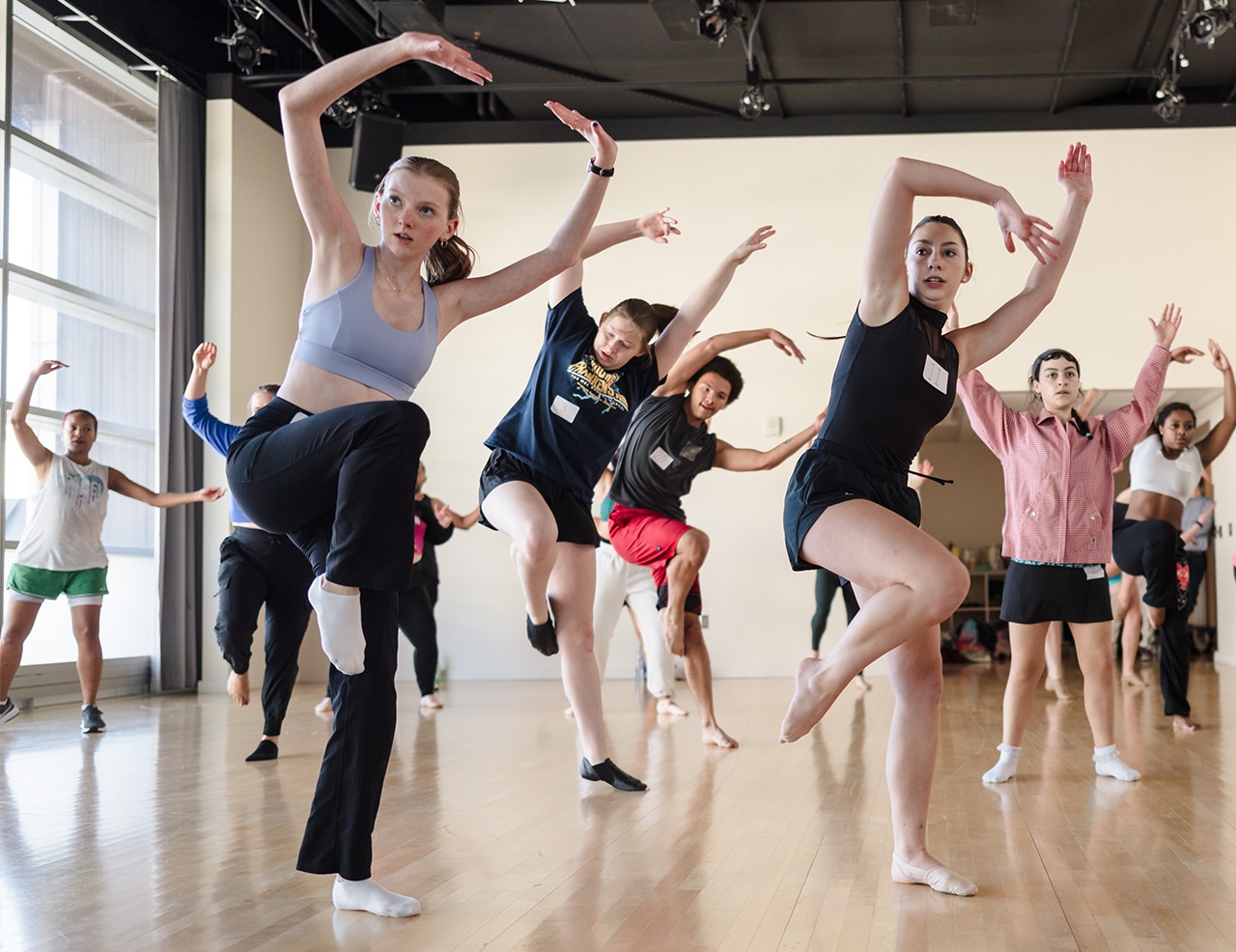 Group of dancers in a studio practicing expressive movements with one knee raised and arms positioned overhead